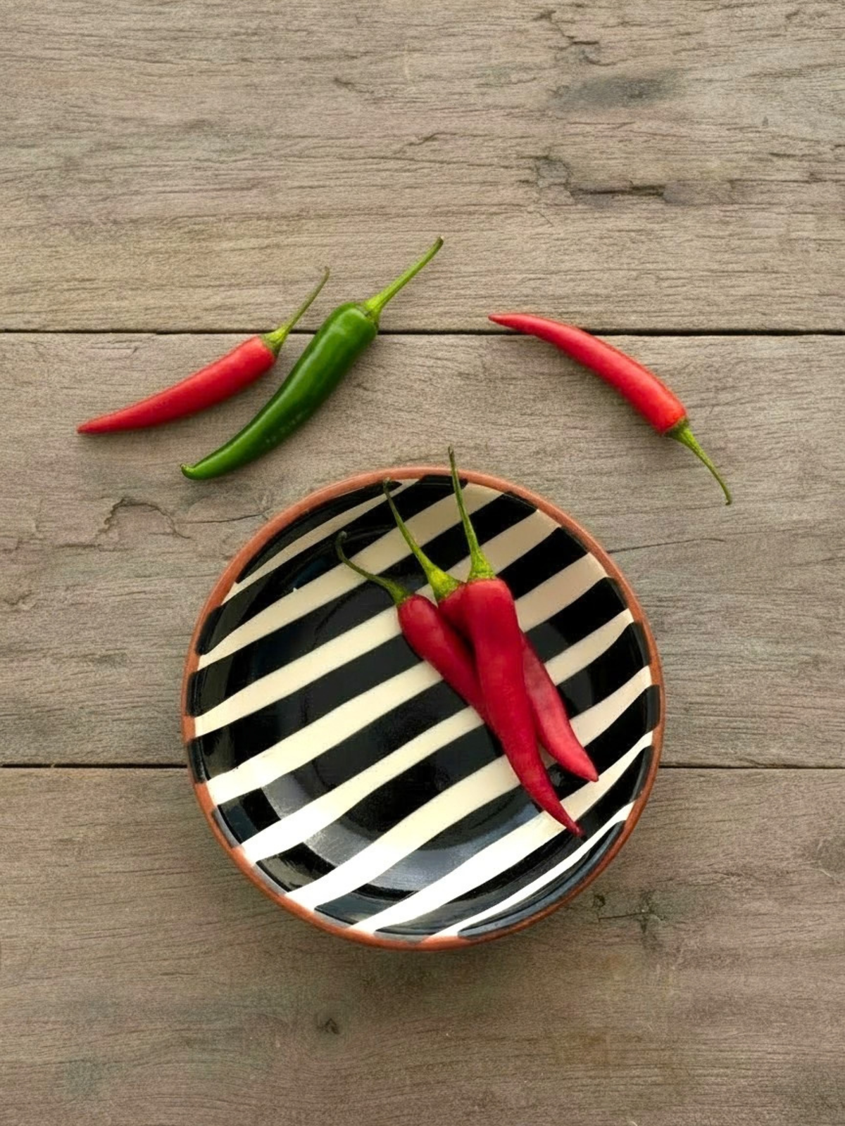 Casa Cubista Bold stripe lille skål i terracotta med hvide og sorte striber på træbord med chili - håndlavet i Portugal