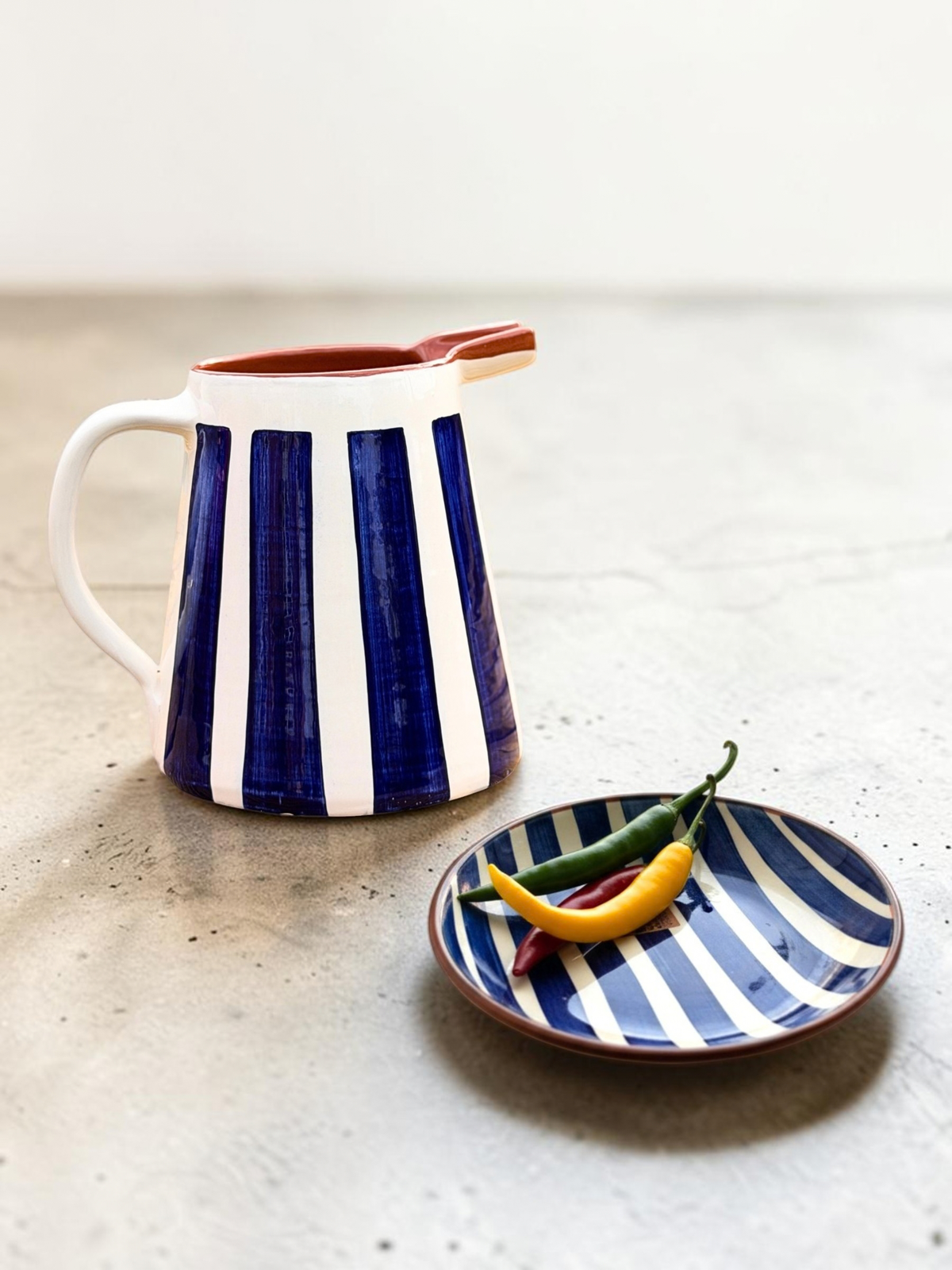 Casa Cubista Bold Stripe blåstribet kande i terracotta sammen med Bold Stripe medium bowl her med chili på - som et sæt. Håndlavet keramik fra Portugal