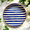 Casa Cubista Bold Stripe blå serveringsskål/fad på hvid overflade med hvide blomster og grønne blade