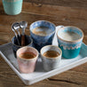 Costa Nova blå og turkis Grespresso keramikkaffekopper og lyserød, sort og grå espressokopper på en bakke